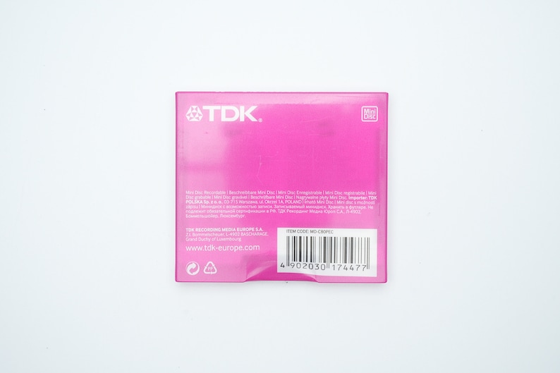 May include: Pink TDK Mini Disc packaging with the text "Mini Disc, Recordable, Rewritable, Mini Disc, Enregistrable, Mini Disc, Rewritable, Mini Disc, gravabile, Mini Disc, riscrivibile, Mini Disc, nagrywalne, Mini Disc, regrav&aacute;vel, Mini Disc, grav&aacute;vel, Mini Disc, перезаписываемый, Mini Disc, записываемый, Mini Disc, قابل إعادة الكتابة, Mini Disc, قابل للتسجيل, TDK POLSKA Sp. z o.o. 71-713 Szczecin ul. Dąbrowskiego 1A, POLAND" and a barcode with the item code "MO-C80PELC".