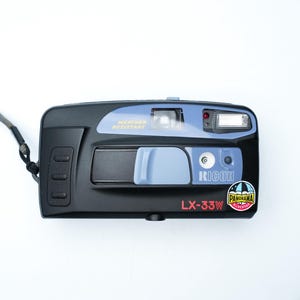 May include: Black and blue Ricoh LX-33W camera with a gray strap. The camera has a flash, a lens, and the text "WEATHER RESISTANT". A sticker on the camera reads "Panorama".