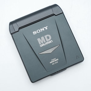 Könnte beinhalten: Ein dunkelgrauer Sony MD Walkman MZ-E32 Digital-Audioplayer. Das Gerät trägt das Sony-Logo und die weißen Worte "MD WALKMAN". Auf der Unterseite des Geräts stehen die Worte "Digital MEGA BASS" und "MZ-E32".