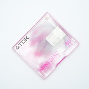 May include: A pink and clear plastic case for a TDK MiniDisc. The case has a label that says "MiniDisc Recordable/Rewritable 80 min".