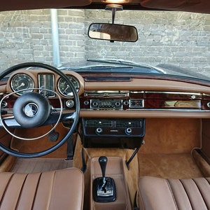 May include: The interior of a vintage car with a brown leather dashboard and seats. The steering wheel is black with a chrome rim. The car has a wooden dashboard with a radio and other controls.
