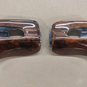 May include: Two brown wood-grain car interior trim pieces with a black plastic insert. The trim pieces are curved and have a glossy finish.