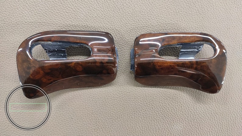 May include: Two brown wood-grain car interior trim pieces with a black plastic insert. The trim pieces are curved and have a glossy finish.