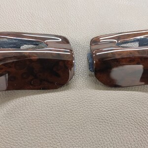 May include: Two brown woodgrain car interior trim pieces with a glossy finish.