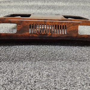 May include: A dark brown, wood-grain effect car interior trim. The trim has a glossy finish and a rectangular shape. It features two rectangular openings and a series of vertical vents in the centre.