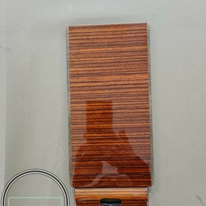 May include: A woodgrain-patterned car interior trim piece with a black handle.