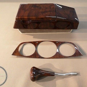 May include: A set of three automotive interior components featuring a glossy dark brown wood grain finish. The set includes a rectangular center console lid, a flat dashboard trim panel with three circular cutouts, and a gear shift knob.