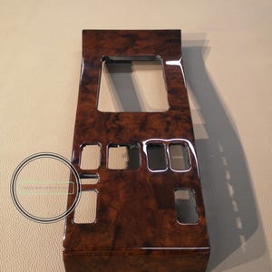 Op de afbeelding: Een donkerbruin houten paneel met een rechthoekige uitsparing en een aantal kleinere rechthoekige uitsparingen. Het paneel heeft een glanzende afwerking.