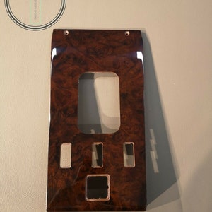 May include: A dark brown wood panel with multiple rectangular cutouts. The panel has a wood grain pattern and a glossy finish.