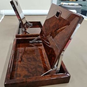 May include: Two wooden trays with hinged lids. The lids are open and the trays have a brown wood grain finish.