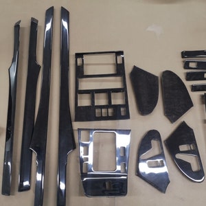 Op de afbeelding: Een set zwarte houtnerf auto-interieurbekledingstukken. De set bevat deurpanelen, dashboardstukken en andere bekledingstukken.