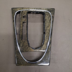 Può includere: Un pezzo di rivestimento interno per auto in legno marrone con una finitura in metallo argentato.