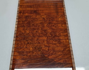 May include: A rectangular, wooden car interior trim piece with a glossy, reddish-brown finish. The trim features horizontal slats and a decorative lower section with a silver accent. The wood grain pattern is visible throughout the piece.