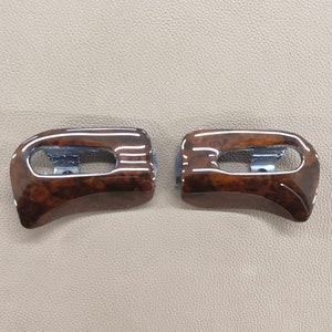 May include: Two brown wood trim pieces with a silver accent. The trim pieces are curved and have a wood grain pattern.