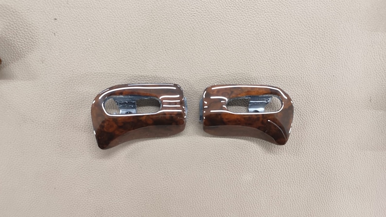 May include: Two brown wood trim pieces with a silver accent. The trim pieces are curved and have a wood grain pattern.