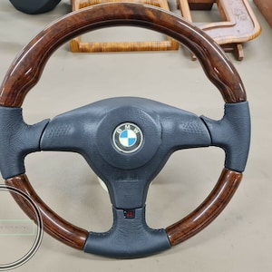 Op de afbeelding: Een donkerbruin houten stuurwiel met een zwarte leren grip en een BMW-logo in het midden.