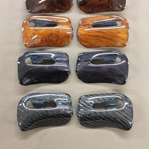 May include: Eight car interior trim pieces in various finishes.  The pieces are made of wood, carbon fiber, and black plastic.  The wood pieces have a brown and orange color.  The carbon fiber pieces have a black and gray color.  The black plastic pieces have a dark purple color.  The pieces are arranged in two rows of four.  The text "wood and carbon works" is visible in the bottom center of the image.