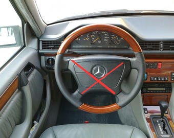 May include: A Mercedes-Benz vehicle interior featuring a steering wheel with a black leather grip and wood grain accents, a central silver star emblem, and a red X mark across the center. The dashboard includes analog gauges and wood trim.