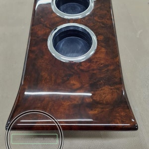 May include: A wooden cup holder with two chrome-rimmed cup holders. The cup holder is brown with a glossy finish.