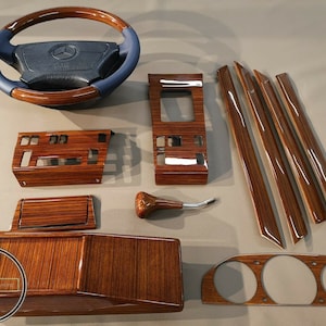 Op de afbeelding: Een set houtnerf auto-interieurbekleding. De set bevat een stuurwiel, dashboardbekleding, deurbekleding en een versnellingspookknop. De bekledingstukken zijn allemaal gemaakt van donker hout met een glanzende afwerking.