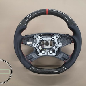May include: A black leather steering wheel with red stitching and a carbon fiber trim. The steering wheel has a red stripe at the top.