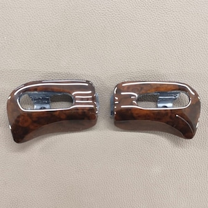 May include: Two brown wood window switch covers with a silver trim. The covers are curved and have a wood grain pattern.