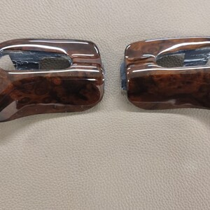May include: Two brown woodgrain car interior trim pieces with a rectangular cutout in the center.