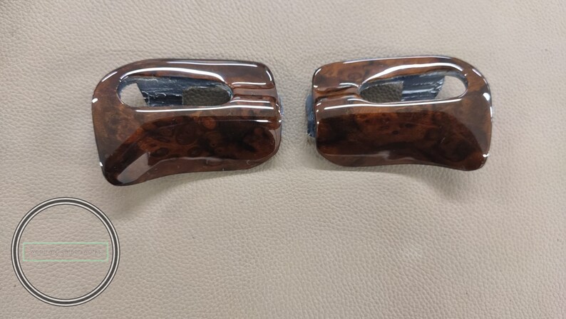 May include: Two brown woodgrain car interior trim pieces with a rectangular cutout in the center.