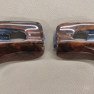 May include: Two brown wood-grain car interior trim pieces with a rectangular cutout in the center.