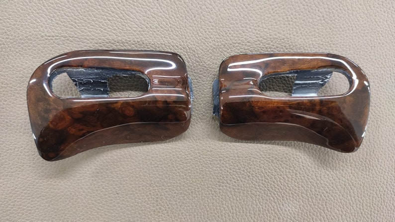 May include: Two brown wood-grain car interior trim pieces with a rectangular cutout in the center.