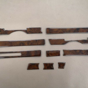 May include: A collection of car interior trim pieces. The pieces are various shapes and sizes, featuring a dark wood grain pattern with a shiny, metallic silver trim. The pieces are arranged on a neutral-colored surface.
