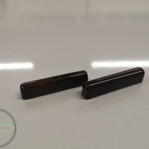 Può includere: Due tiretti per cassetti in legno marrone scuro con una finitura liscia e lucida.