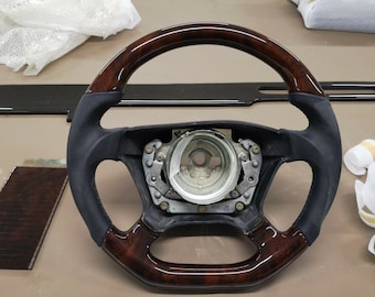 May include: A dark brown wood steering wheel with black leather accents. The steering wheel has a silver center hub with a black plastic ring around it.