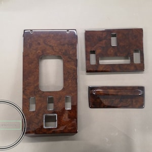 May include: Set of four woodgrain car interior trim pieces. The pieces are rectangular and have a brown woodgrain finish with silver accents. The pieces are designed to fit in a car's interior.