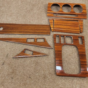 Op de afbeelding: Een set van zes houten auto-interieurbekledingstukken. De stukken zijn in verschillende vormen en maten en hebben een bruine houtnerf.