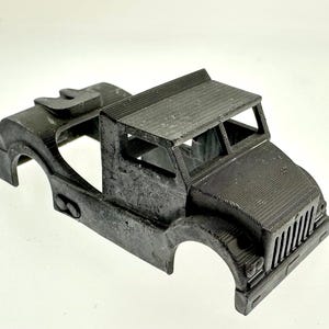 Pode incluir: Uma cabine de caminh&atilde;o modelo de pl&aacute;stico preto com uma grelha frontal detalhada e um teto elevado. A cabine n&atilde;o tem ca&ccedil;amba nem rodas.