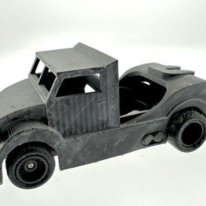 Pode incluir: Um caminh&atilde;o de brinquedo de pl&aacute;stico preto com um reboque de plataforma. O caminh&atilde;o tem uma cabine detalhada com um p&aacute;ra-brisa e um teto. O reboque est&aacute; vazio e tem um engate na parte traseira.