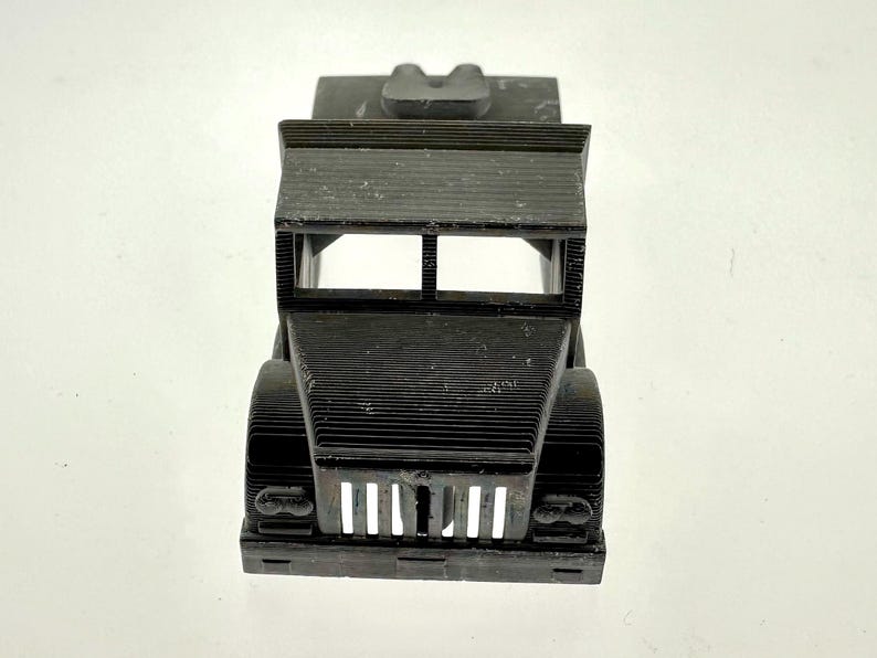 Pode incluir: Um modelo de caminh&atilde;o de brinquedo de pl&aacute;stico preto com uma grelha frontal e far&oacute;is detalhados. O caminh&atilde;o tem uma plataforma e &eacute; feito com uma impressora 3D.