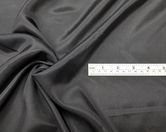 May include: A close-up of a dark gray fabric with a smooth, silky texture. A ruler is placed on top of the fabric, showing measurements in inches.