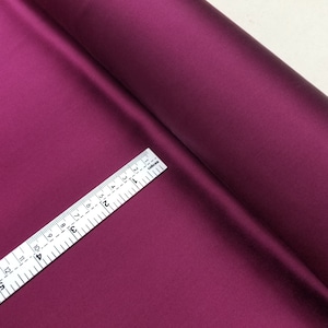 May include: A roll of deep burgundy satin fabric with a white measuring tape on top. The tape measures 38 cm.