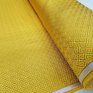 May include: A roll of gold fabric with a geometric pattern. The fabric has a subtle sheen and a textured surface.