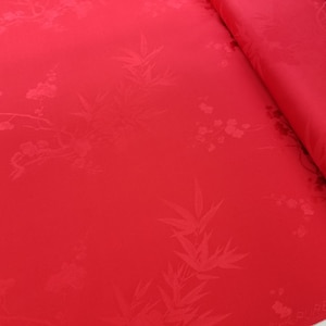 Pode incluir: Tecido vermelho com um padrão em relevo sutil de bambu e flores de cerejeira. O tecido está enrolado e a borda é visível.