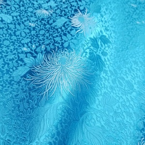 May include: A close-up of a blue fabric with a white floral pattern. The fabric has a subtle sheen and a textured surface.