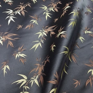 Peut inclure: Tissu noir orné d'un motif de feuilles de bambou dans des tons de marron, crème et vert. Le tissu présente un léger éclat, suggérant du satin ou de la soie. Les feuilles sont disposées dans un motif naturel et fluide.