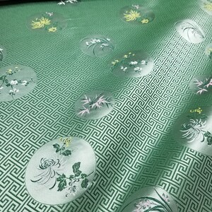以下が含まれることがあります： 円の中にギリシャの鍵のデザインと花のモチーフが繰り返されるパターンが施された緑色の生地。生地は控えめな光沢があります。