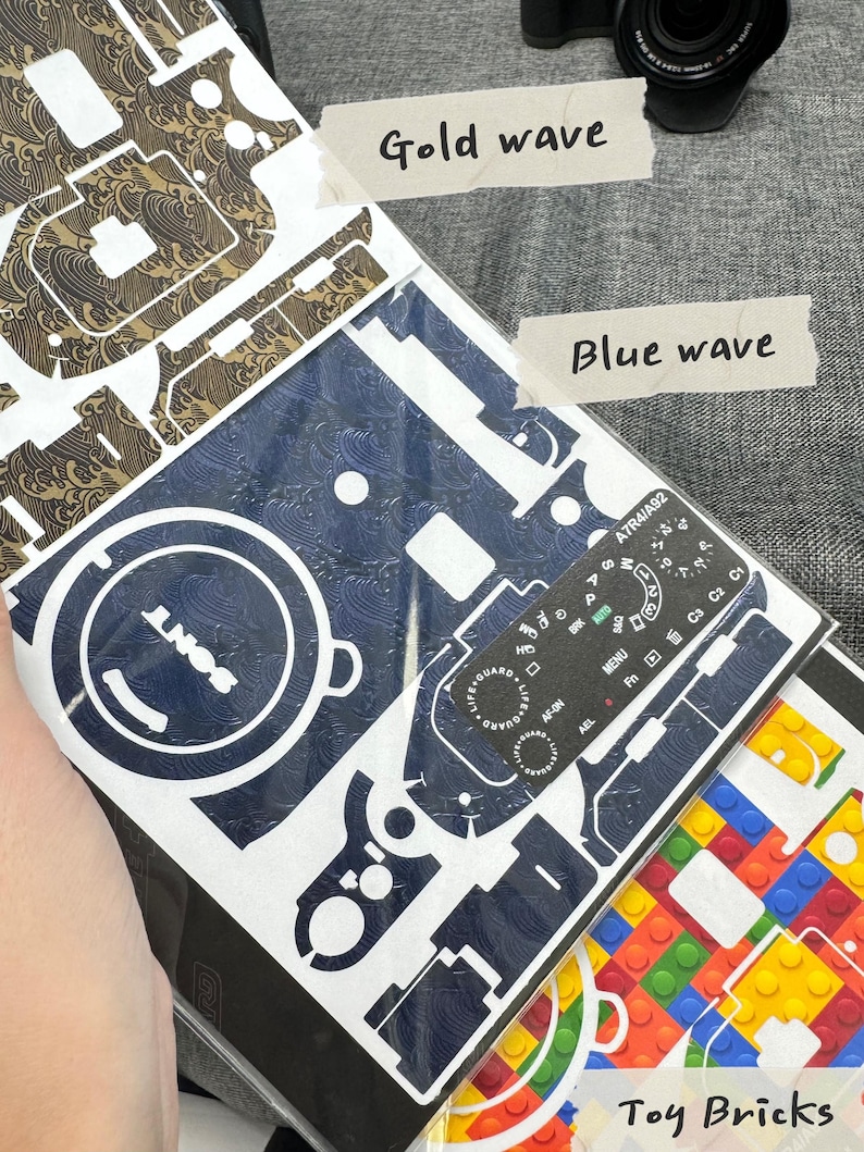 May include: Three camera skin designs: a gold wave pattern, a blue wave pattern, and a colourful toy brick pattern. The designs are printed on white paper and are ready to be applied to a camera.