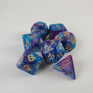 Könnte beinhalten: Ein Satz von sieben Würfeln mit einem blauen und violetten Marmormuster und goldenen Zahlen. Die Würfel haben verschiedene Formen, darunter einen Würfel, eine Pyramide und ein Tetraeder.