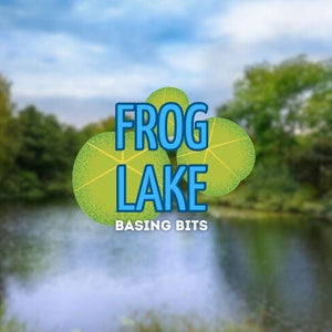 May include: A green and blue logo with the text "FROG LAKE" and the words "BASING BITS" below. The logo is set against a blurred background of a lake and trees.
