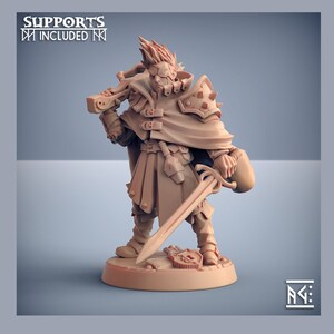 Op de afbeelding: Een 3D-geprint miniatuur van een fantasyfiguur, een mannelijke mens met stekelig blond haar, die een bruin leren jack, een donkere mantel draagt en een zwaard en een kruisboog vasthoudt. Het miniatuur is geschilderd in een lichtbruine kleur.