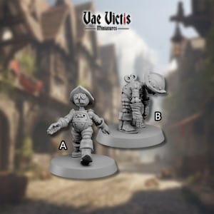 Könnte beinhalten: Zwei graue, detaillierte Miniaturfiguren von Robotern in verschiedenen Posen. Der Roboter links steht mit ausgestrecktem Arm, während der Roboter rechts mit gekreuzten Armen gebeugt ist. Beide Roboter tragen Helme und haben eine Steampunk-Ästhetik. Der Text "Vae Victis Miniatures" ist oben im Bild sichtbar.